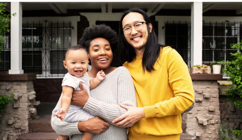 Man and woman couple holding their baby, all smiling at the camera.