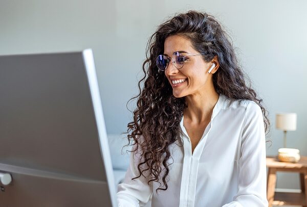 Woman wearing AirPods, smiling while looking at her computer screen.