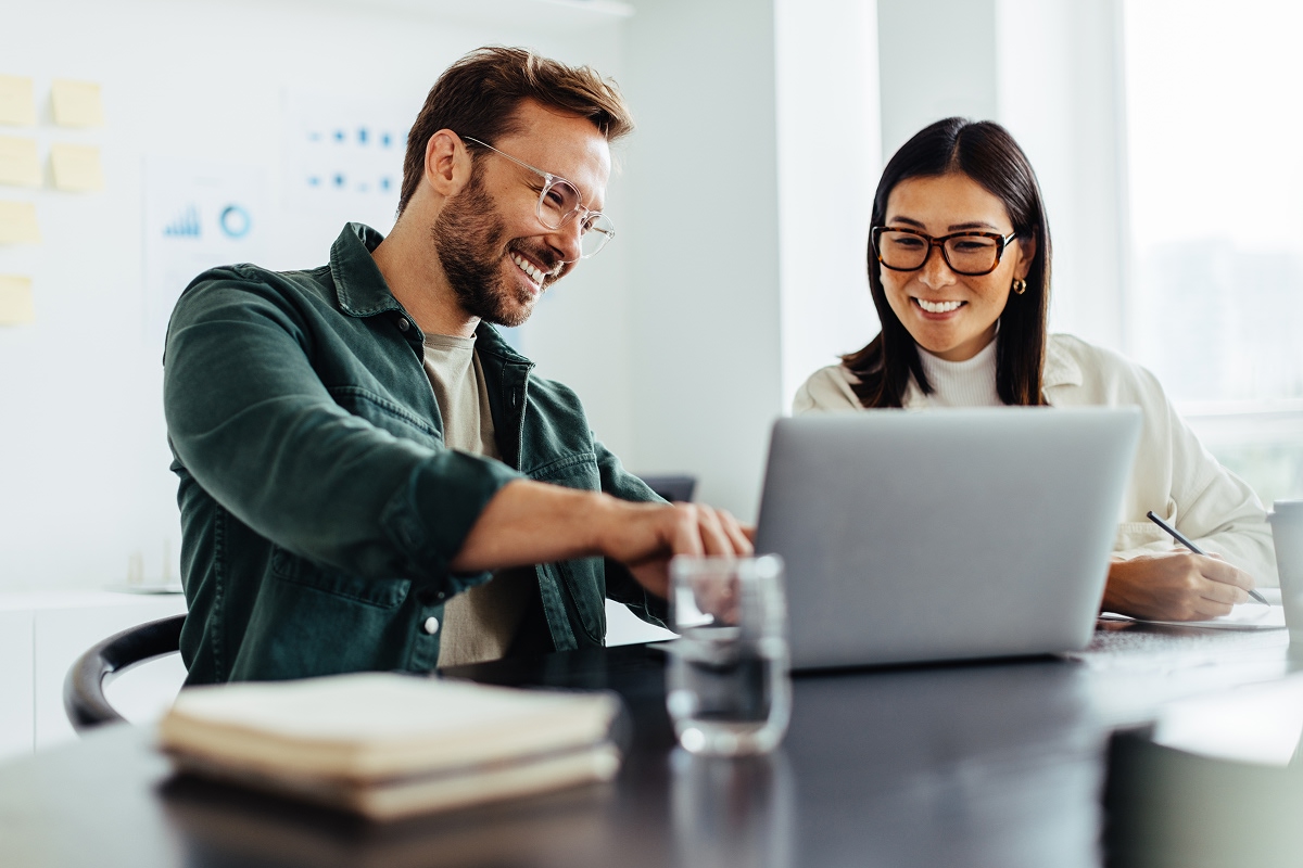 Man and woman smiling while looking at a laptop screen.