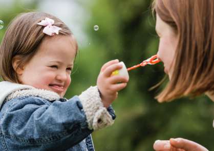 Little girl holding a bubble wand, showing it to an adult.