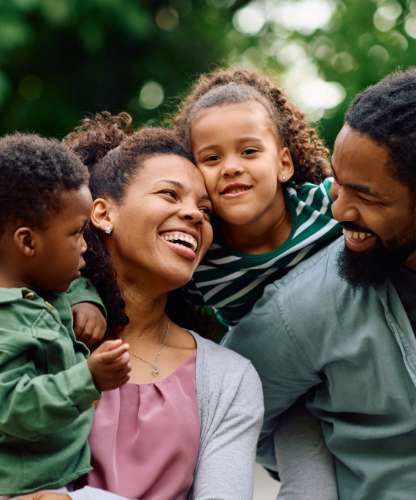 A boy being carried by his mother, a little girl on her father's back, both parents smiling at each other.
