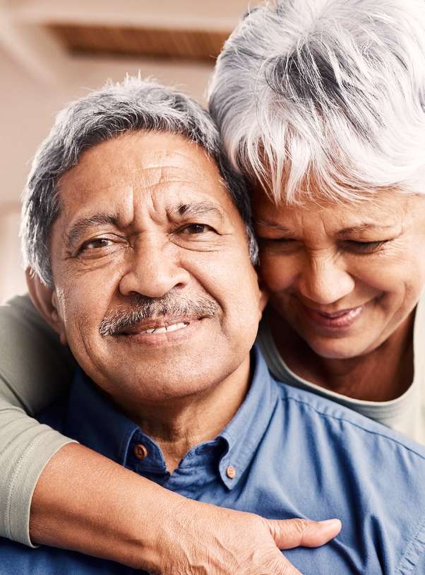 A woman embracing a man who is looking into the camera with a small smile.
