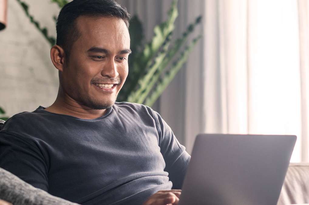 Man sitting and smiling while looking at his laptop.